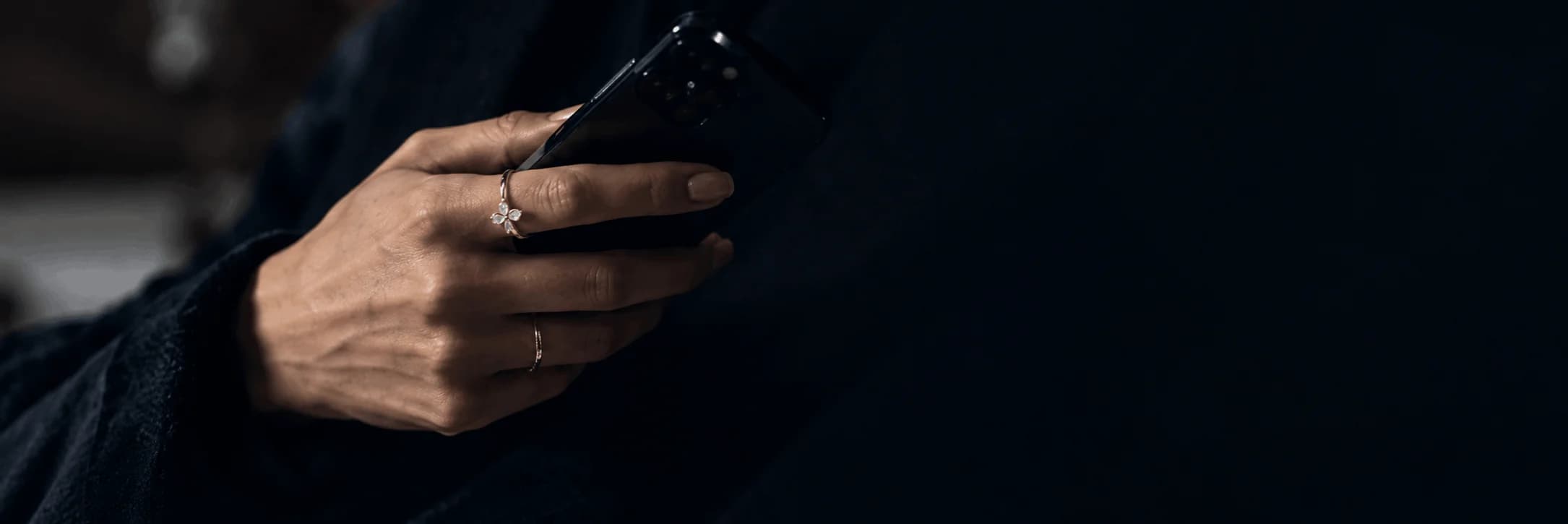 Hands holding smartphone wearing delicate Azor stack rings